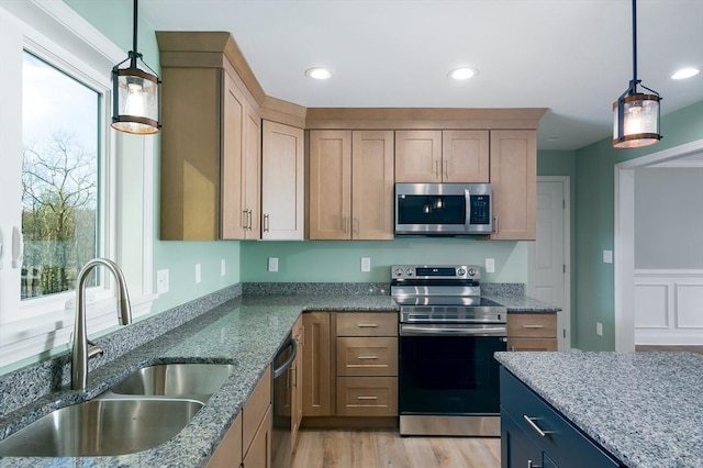 kitchen featuring dark stone counters, sink, appliances with stainless steel finishes, decorative light fixtures, and light hardwood / wood-style floors