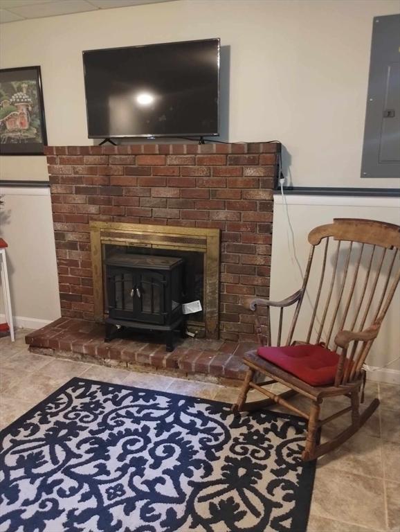 sitting room featuring a wood stove, electric panel, and tile patterned floors