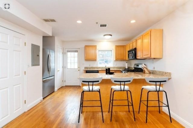 kitchen featuring appliances with stainless steel finishes, light brown cabinets, a kitchen breakfast bar, and kitchen peninsula