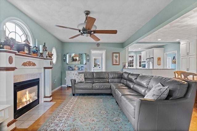 living room with light wood-type flooring, ceiling fan, and a tiled fireplace