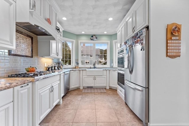 kitchen with white cabinetry, custom exhaust hood, stainless steel appliances, light stone countertops, and sink