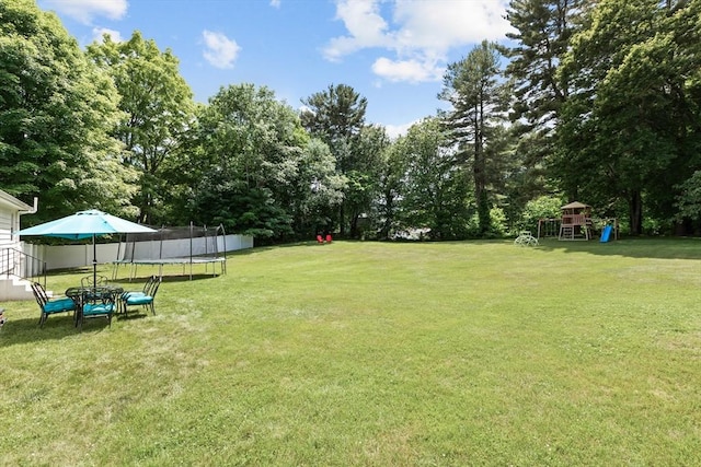 view of green lawn with a trampoline, a playground, and view of scattered trees