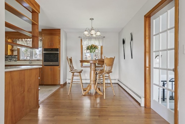 dining area with a chandelier, light wood finished floors, a baseboard heating unit, and baseboard heating