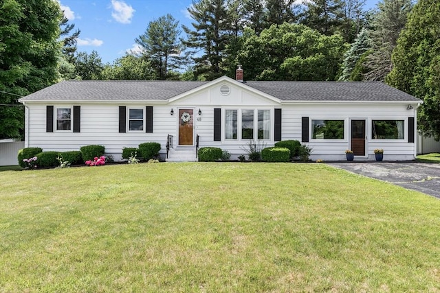ranch-style home with entry steps, a front yard, roof with shingles, and a chimney