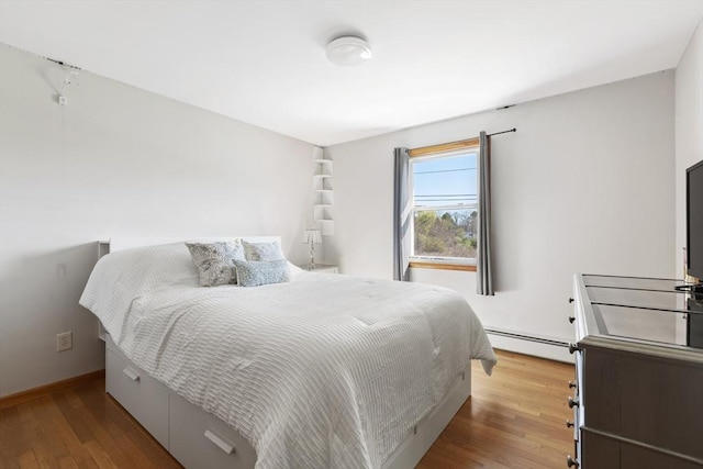 bedroom with a baseboard radiator, wood finished floors, and baseboards