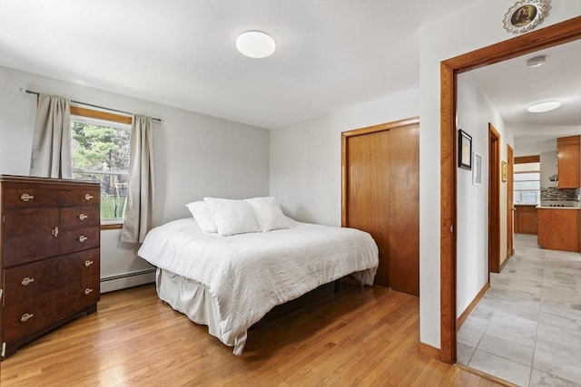 bedroom featuring a baseboard heating unit, light wood-style flooring, and baseboards