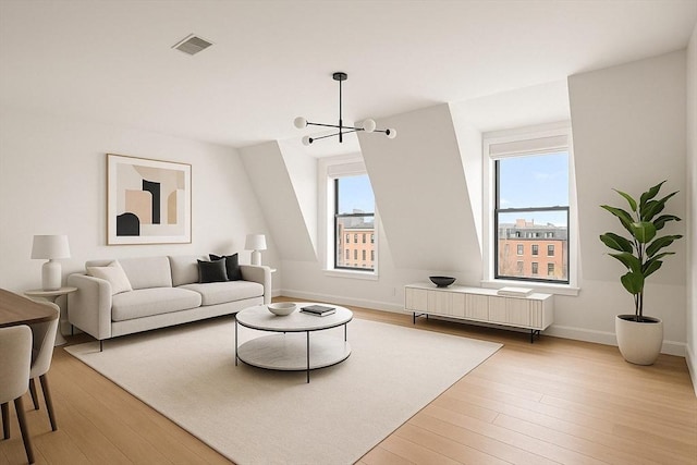 living area with an inviting chandelier, visible vents, light wood finished floors, and a healthy amount of sunlight