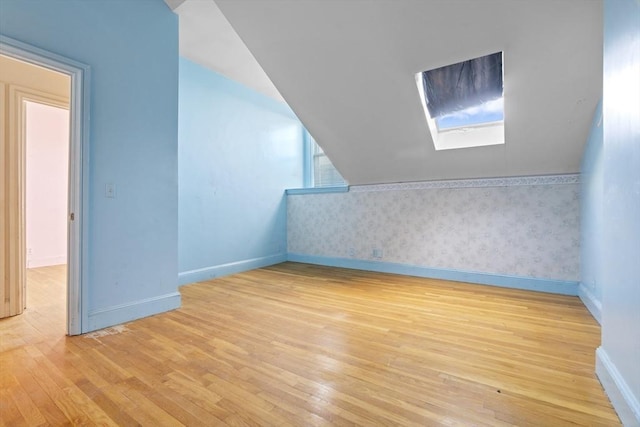 bonus room with lofted ceiling with skylight, hardwood / wood-style flooring, and baseboards
