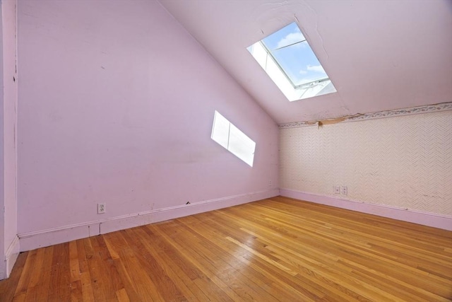 additional living space with light wood-style flooring, baseboards, and lofted ceiling with skylight
