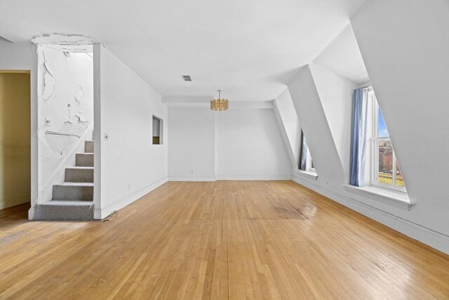 additional living space featuring stairs, a chandelier, light wood-style floors, and visible vents