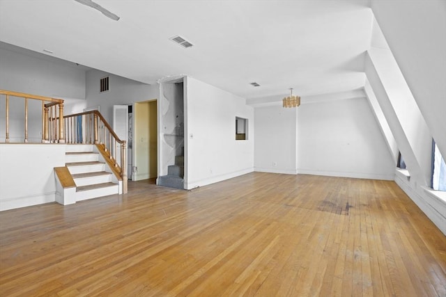 unfurnished living room featuring light wood-type flooring, baseboards, visible vents, and stairway