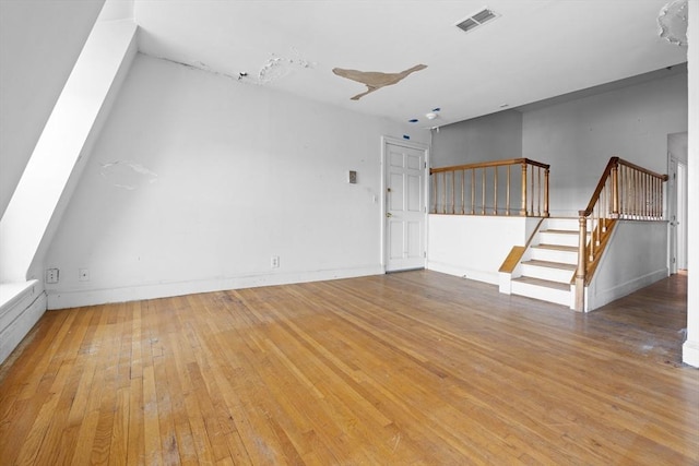unfurnished living room featuring light wood-type flooring, visible vents, baseboards, and stairway
