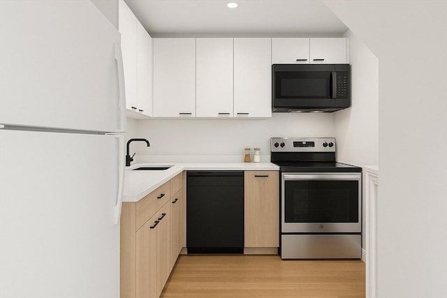kitchen featuring light wood finished floors, light countertops, a sink, black appliances, and white cabinetry
