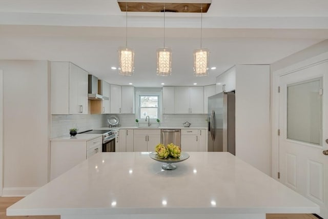 kitchen featuring backsplash, appliances with stainless steel finishes, white cabinetry, light countertops, and wall chimney exhaust hood