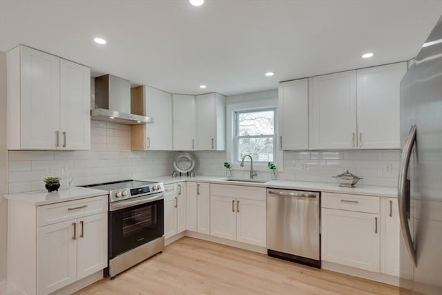 kitchen with white cabinets, a sink, wall chimney exhaust hood, stainless steel appliances, and tasteful backsplash