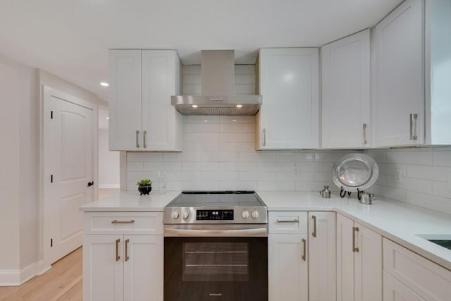 kitchen with backsplash, stainless steel range with electric cooktop, white cabinetry, and wall chimney exhaust hood