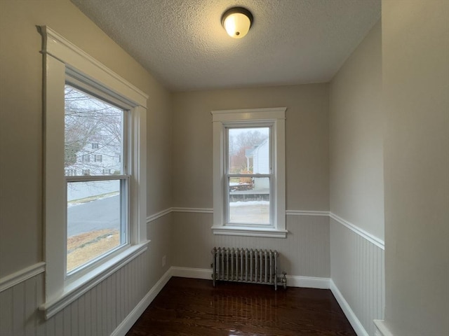 spare room with radiator, plenty of natural light, dark hardwood / wood-style floors, and a textured ceiling