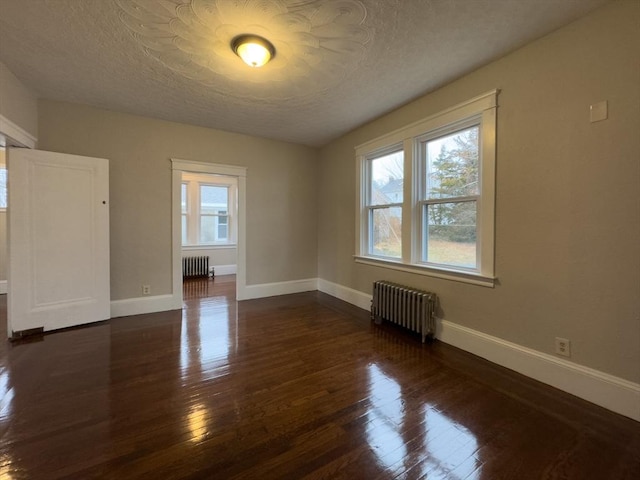 empty room featuring dark wood-type flooring, radiator heating unit, and plenty of natural light