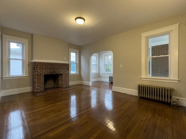 unfurnished living room with radiator heating unit, dark hardwood / wood-style flooring, and a brick fireplace