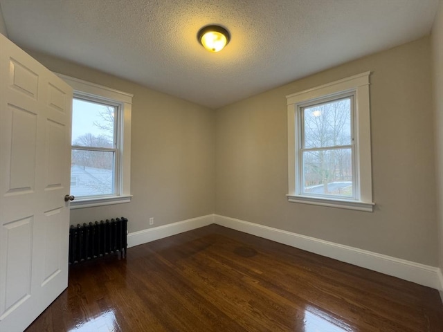 empty room featuring dark hardwood / wood-style flooring, radiator, a wealth of natural light, and a textured ceiling