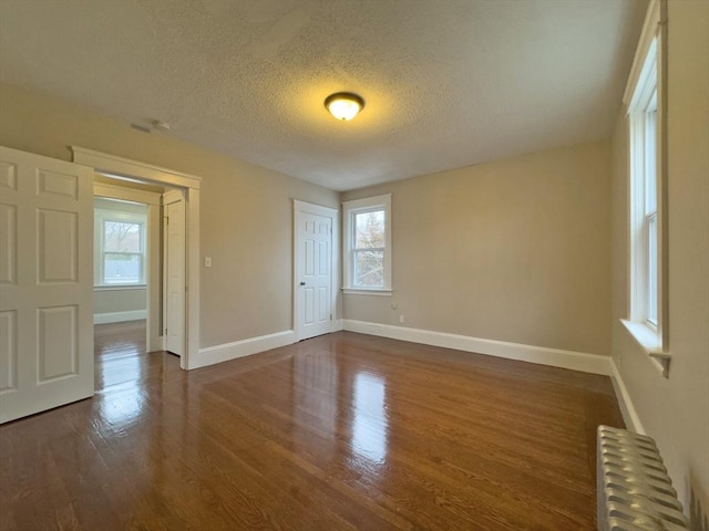 empty room featuring dark hardwood / wood-style flooring, radiator, and a textured ceiling