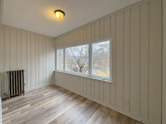 spare room featuring light hardwood / wood-style flooring, radiator heating unit, and a textured ceiling