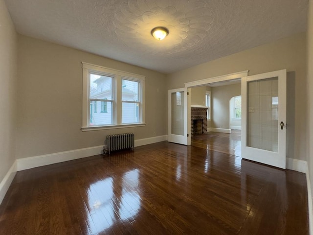 unfurnished living room featuring dark wood-type flooring, french doors, a textured ceiling, radiator heating unit, and a fireplace