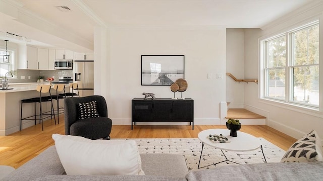 living area with ornamental molding, light wood-type flooring, visible vents, and baseboards