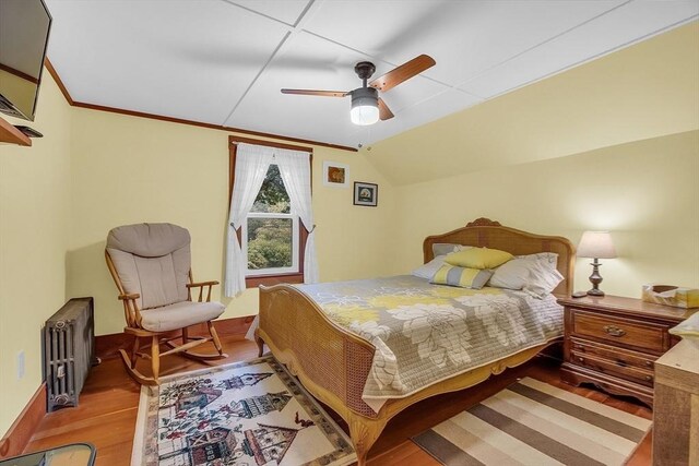 bedroom with hardwood / wood-style flooring, ornamental molding, vaulted ceiling, radiator heating unit, and ceiling fan