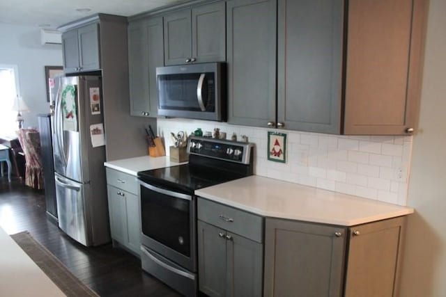 kitchen featuring appliances with stainless steel finishes, gray cabinetry, a wall mounted AC, decorative backsplash, and dark hardwood / wood-style floors