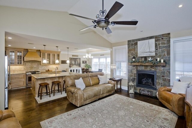 living area with recessed lighting, a stone fireplace, dark wood-type flooring, lofted ceiling, and ceiling fan with notable chandelier