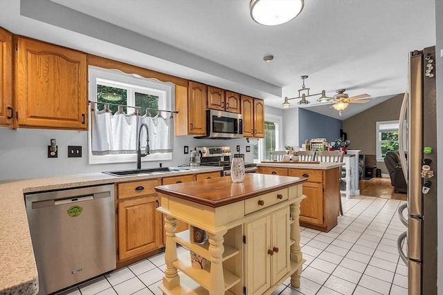 kitchen with ceiling fan, sink, stainless steel appliances, light tile patterned floors, and a kitchen island