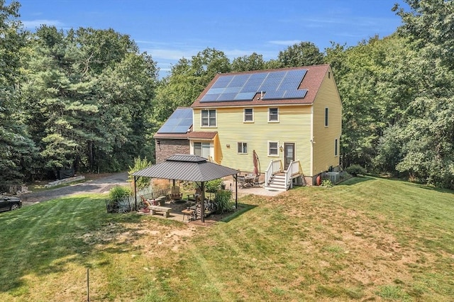 rear view of property featuring a gazebo, solar panels, a patio area, and a lawn