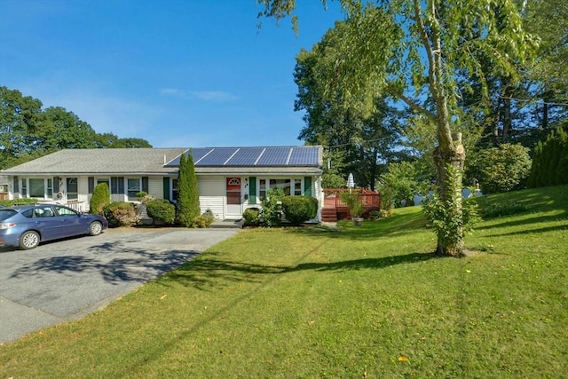 ranch-style house with roof mounted solar panels, asphalt driveway, and a front yard