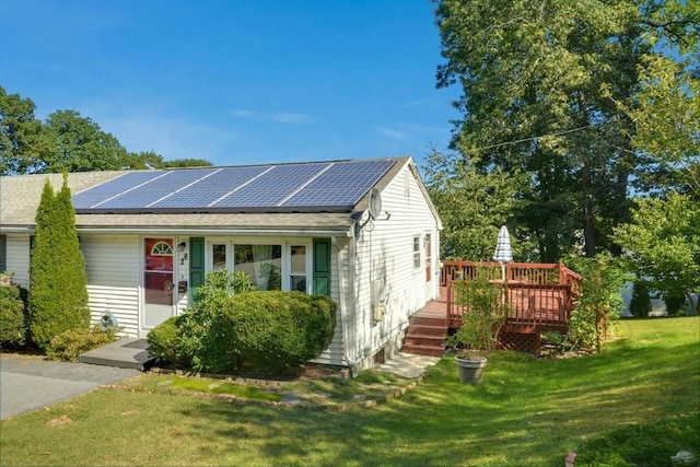 view of front of property with a front lawn, solar panels, a deck, and roof with shingles