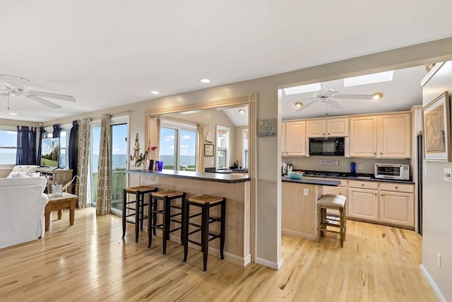125 Seaview Dr, Plymouth, MA 02360 - kitchen with light brown cabinets, vaulted ceiling with skylight, black microwave, a kitchen bar, and dark countertops