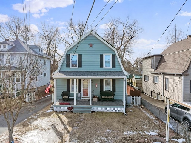 dutch colonial with covered porch, a shingled roof, fence, and a gambrel roof