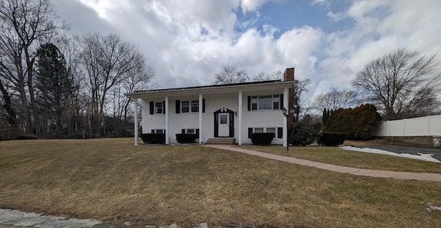 bi-level home with entry steps, a front yard, fence, and a chimney