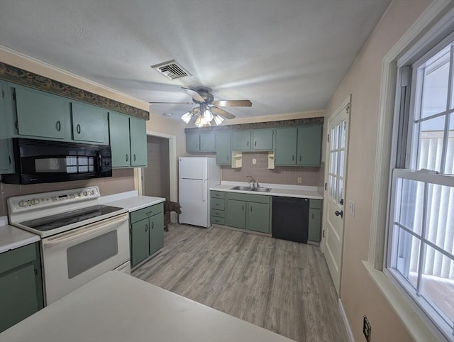 kitchen with visible vents, green cabinetry, a sink, decorative backsplash, and black appliances