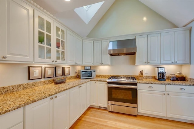 kitchen with stainless steel appliances, a skylight, white cabinetry, wall chimney exhaust hood, and light wood finished floors