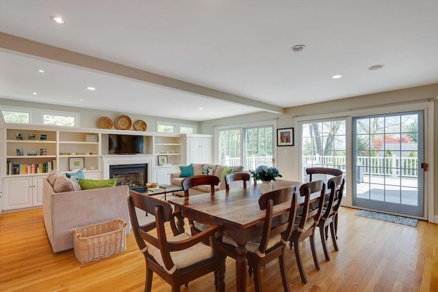 dining space with light wood-style floors, a glass covered fireplace, beamed ceiling, and recessed lighting