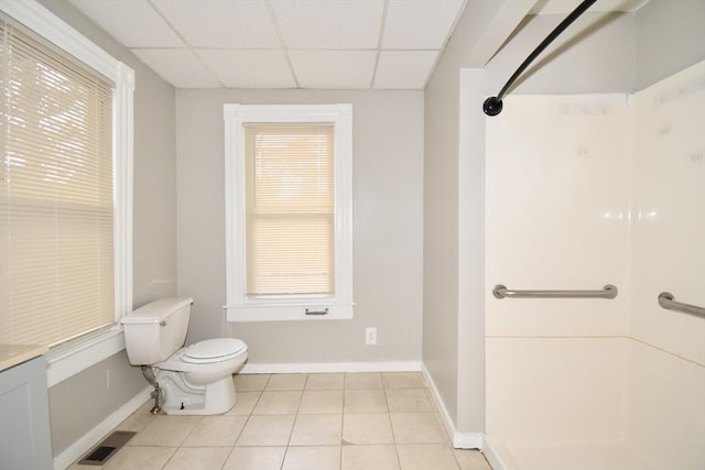 bathroom featuring tile patterned flooring, a drop ceiling, a healthy amount of sunlight, and toilet