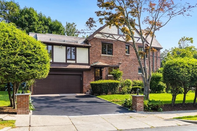 tudor house with a garage, driveway, brick siding, and stucco siding