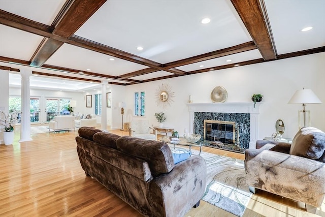 living area featuring coffered ceiling, beamed ceiling, light wood-type flooring, ornate columns, and a high end fireplace