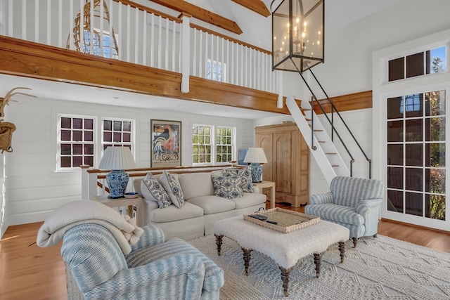 living room featuring wood-type flooring, a chandelier, a high ceiling, and beam ceiling