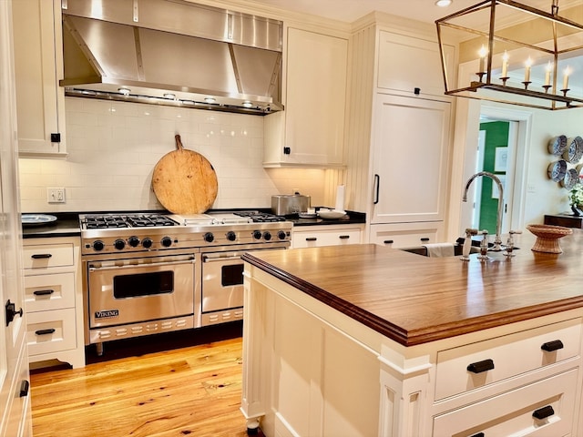 kitchen featuring premium stove, light wood-type flooring, wooden counters, decorative backsplash, and wall chimney exhaust hood