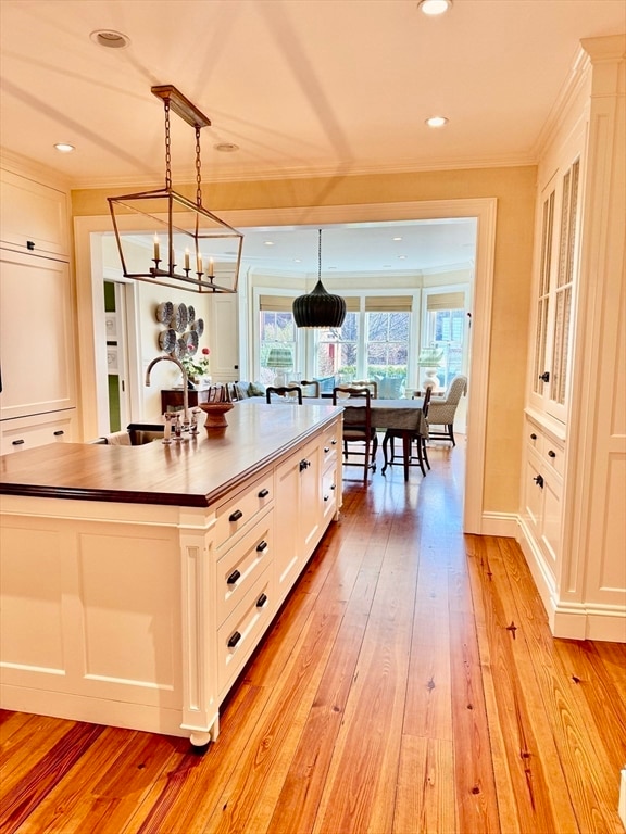 kitchen with light hardwood / wood-style floors, a center island with sink, white cabinetry, decorative light fixtures, and a chandelier