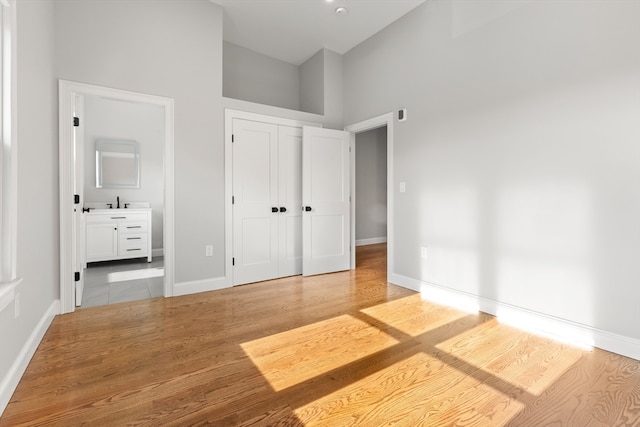 unfurnished bedroom featuring a closet, ensuite bath, wood-type flooring, and a high ceiling