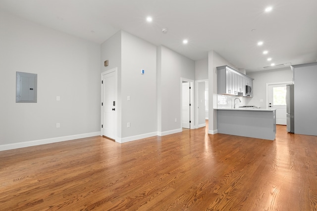 unfurnished living room with sink, electric panel, and light wood-type flooring