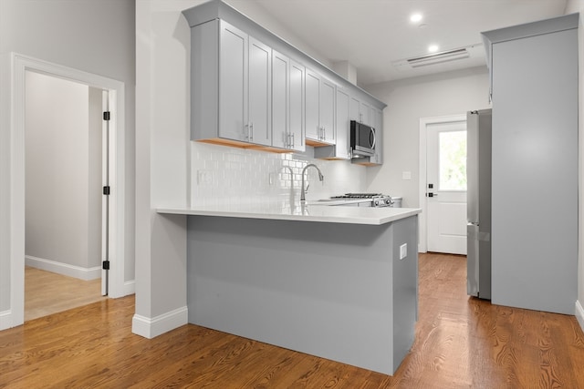 kitchen featuring appliances with stainless steel finishes, light wood-type flooring, backsplash, kitchen peninsula, and gray cabinets